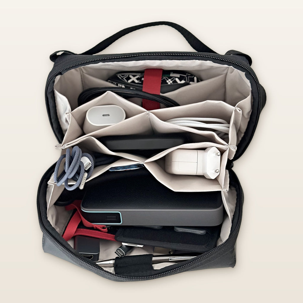 Organizer tech aperto con caricatore, powerbank e cavi nelle tasche a soffietto